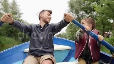 快乐的父子抱着桨在湖上划船。 开心的爸爸和小朋友说说笑笑.. 年轻的父亲